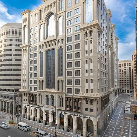 Al Aqeeq Madinah Hotel Médine Extérieur photo The photo depicts a large, modern building with a distinctive architectural style. The structure shows a blend of classic and contemporary design elements, featuring ornate details, large glass windows, and a prominent central facade. Surrounding the
