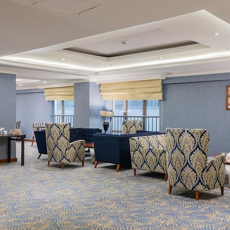 Al Aqeeq Madinah Hotel Médine Extérieur photo The photo shows a stylish indoor lounge or sitting area. It features several upholstered armchairs arranged around a central space. The chairs have a blue and cream patterned upholstery, creating a sophisticated ambiance. There is a table alongside s