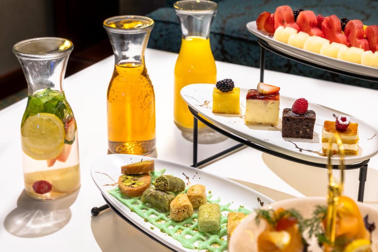 Al Aqeeq Madinah Hotel Médine Extérieur photo The photo showcases an elegant display of refreshments and desserts. There are several glass pitchers filled with bright, colorful beverages, likely juices or infused water, one featuring lemon and mint. A two-tier serving stand holds an assortment o