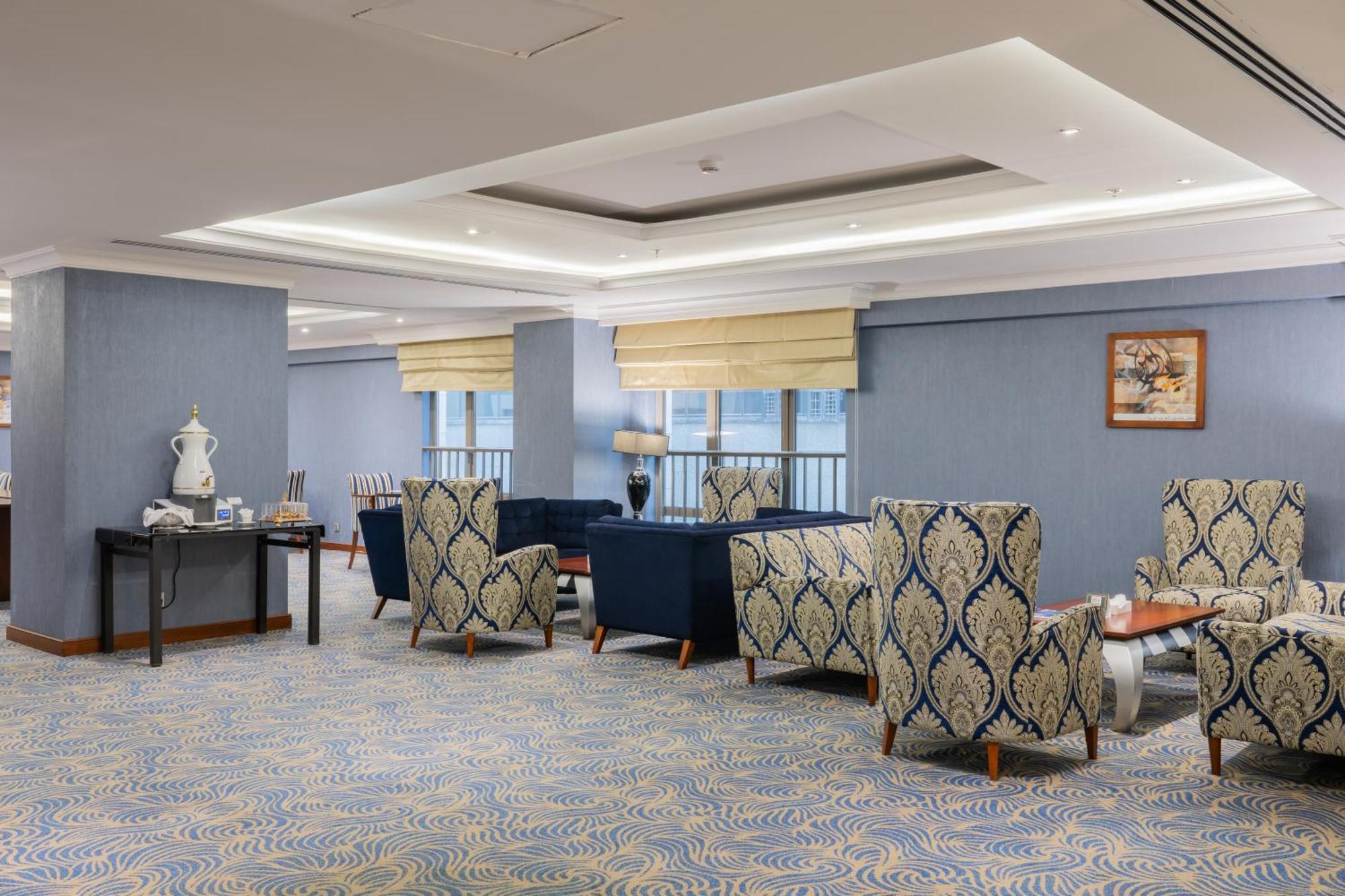 Al Aqeeq Madinah Hotel Médine Extérieur photo The photo shows a stylish indoor lounge or sitting area. It features several upholstered armchairs arranged around a central space. The chairs have a blue and cream patterned upholstery, creating a sophisticated ambiance. There is a table alongside s