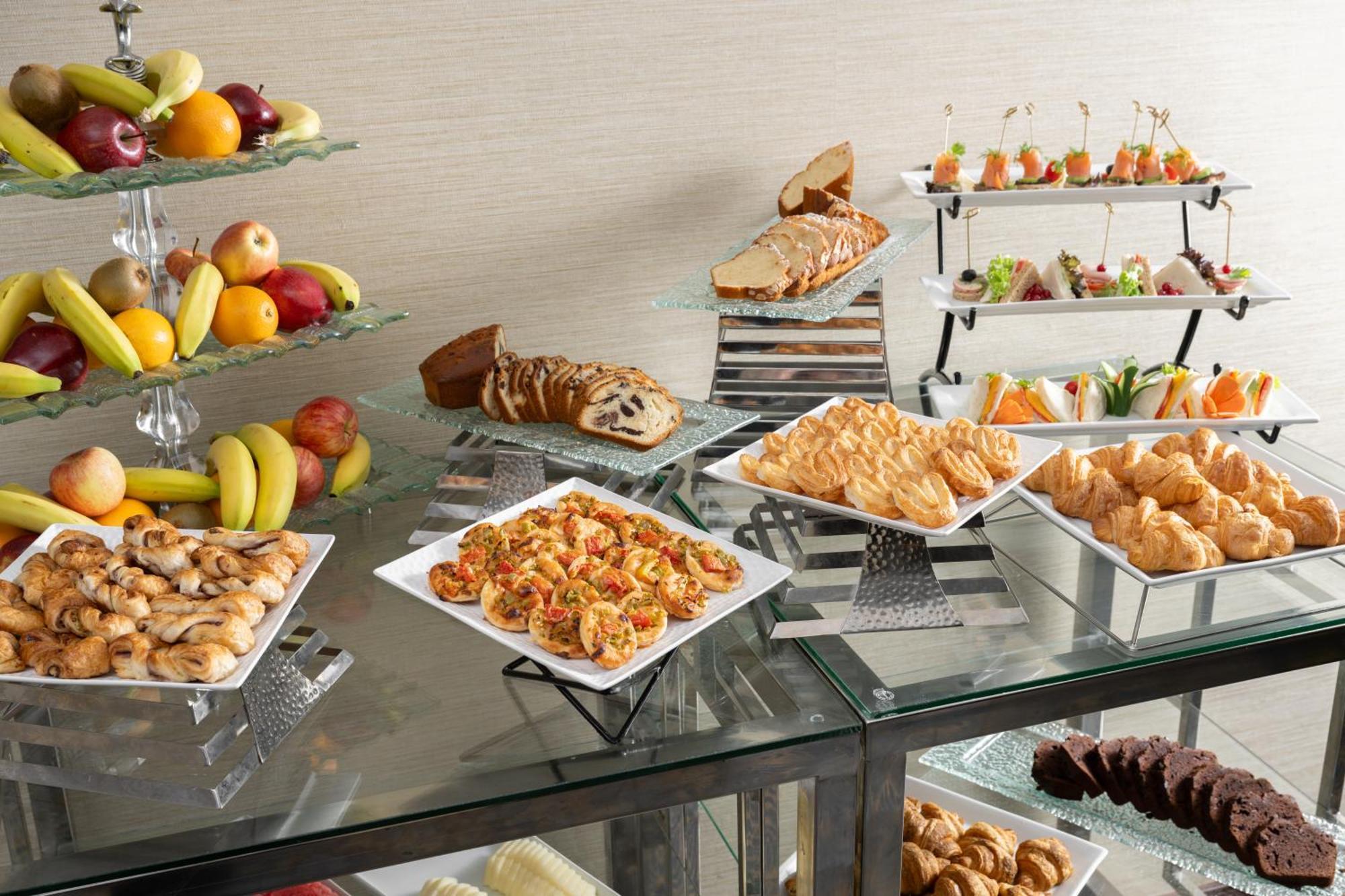 Al Aqeeq Madinah Hotel Médine Extérieur photo The photo showcases a buffet-style spread featuring a variety of food items. There are several platters with appetizers, including seafood dishes, pastries, and other savory items. In addition, there is a selection of fresh fruit displayed on a glass
