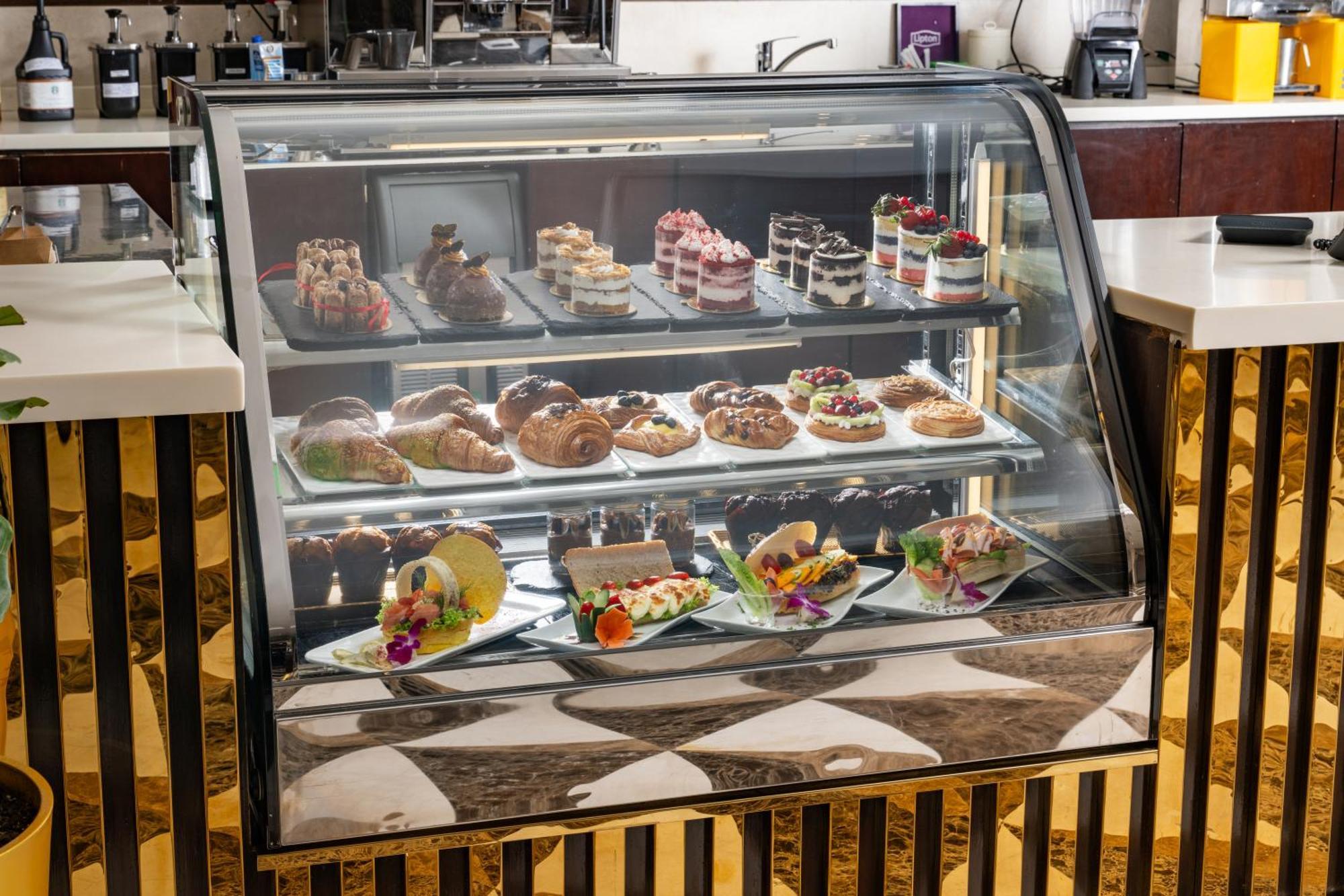 Al Aqeeq Madinah Hotel Médine Extérieur photo The photo shows a display case filled with an assortment of desserts. There are various types of pastries, including cakes, tarts, and croissants, arranged neatly on different shelves. The desserts are visually appealing, with colorful decorations, f