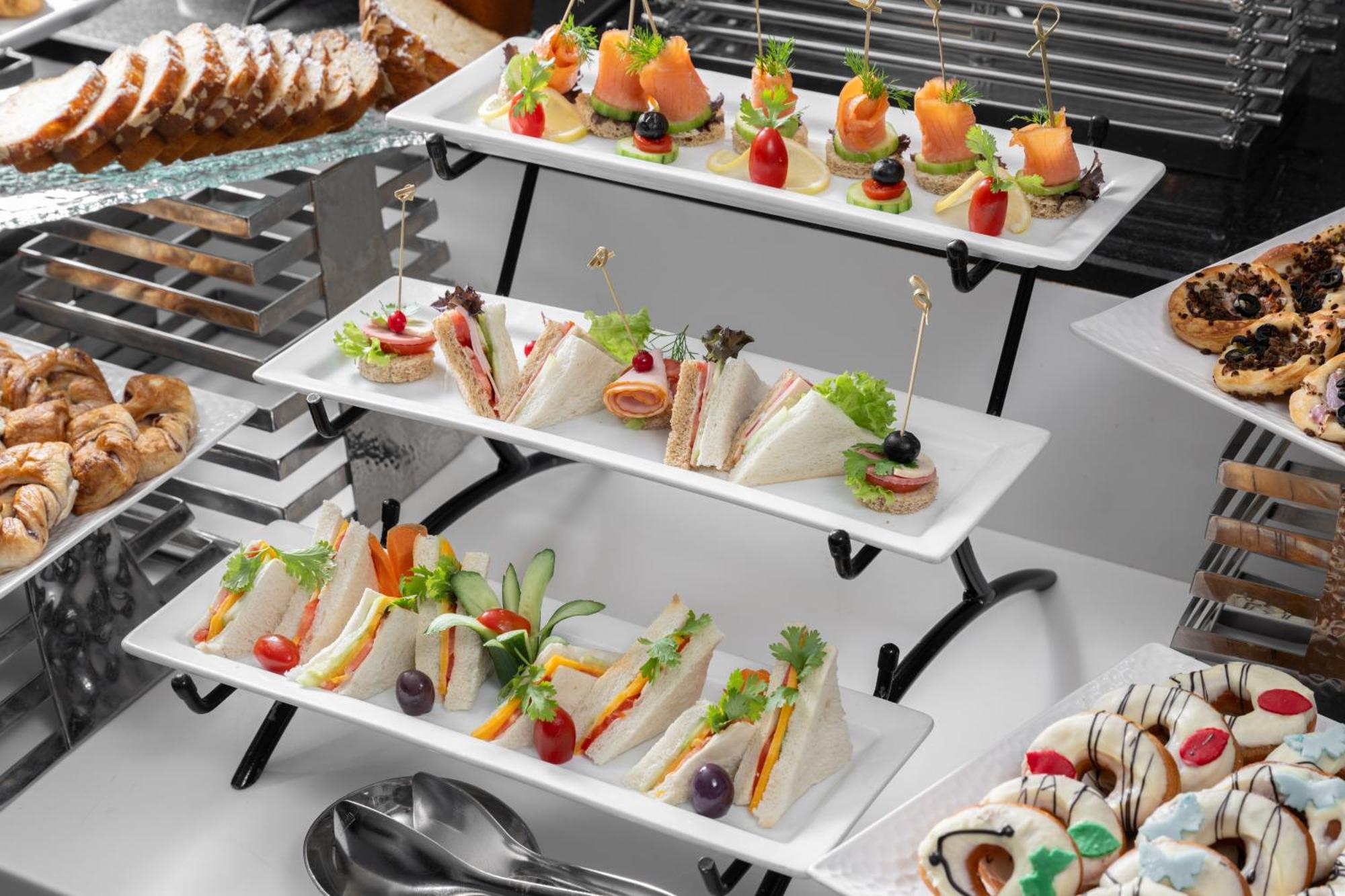 Al Aqeeq Madinah Hotel Médine Extérieur photo The photo shows a tiered display of assorted appetizers and snacks arranged on white rectangular plates. 

1. **Top Tier**: Contains small bites featuring smoked salmon garnished with greenery, and some with colorful cherry tomatoes on toothpicks. 

