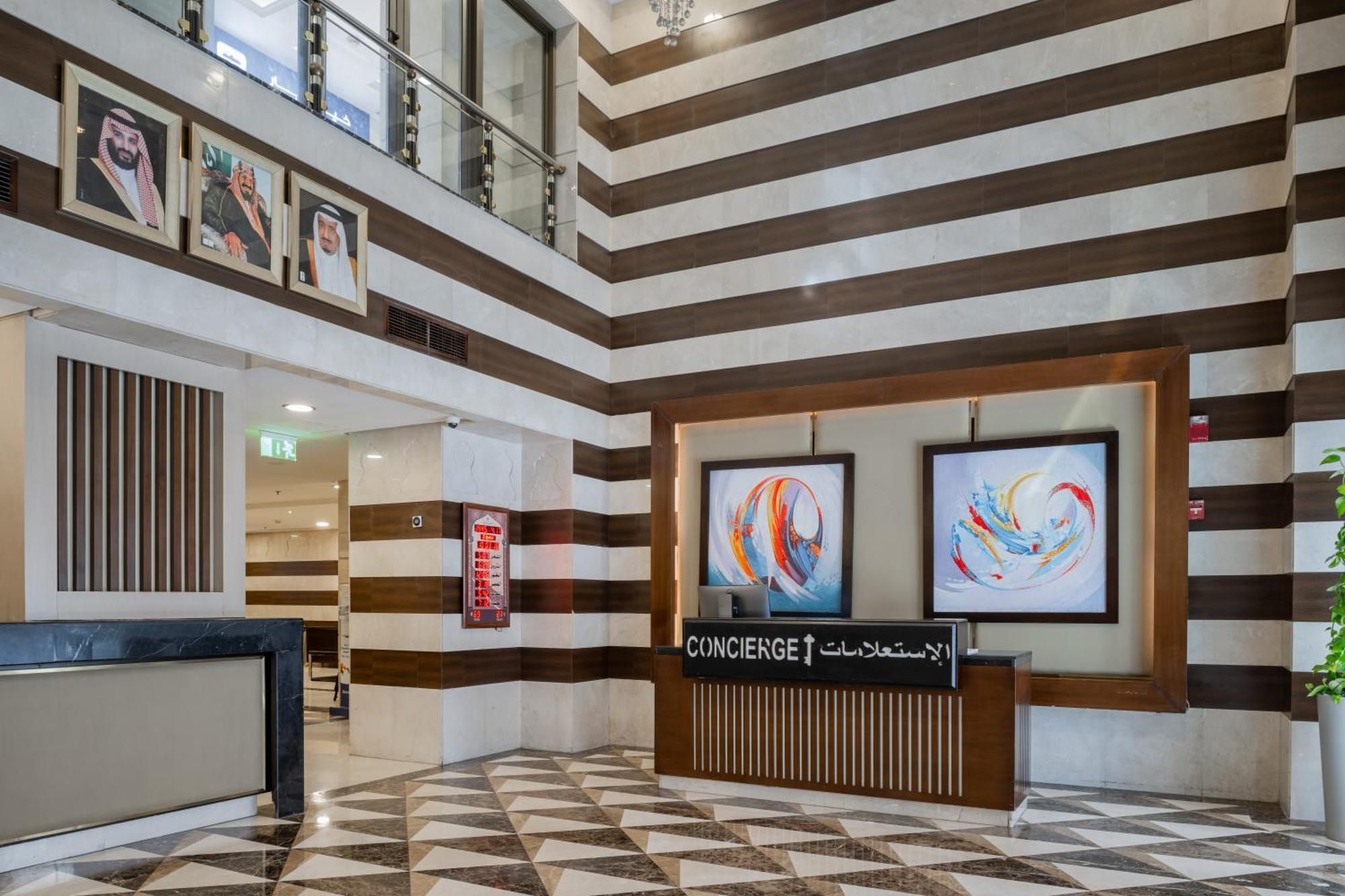Al Aqeeq Madinah Hotel Médine Extérieur photo The photo shows a modern hotel lobby area characterized by its stylish design. The walls feature a pattern of horizontal stripes in different shades, creating a sophisticated atmosphere. To the left, there is a reception area with a sleek desk labele