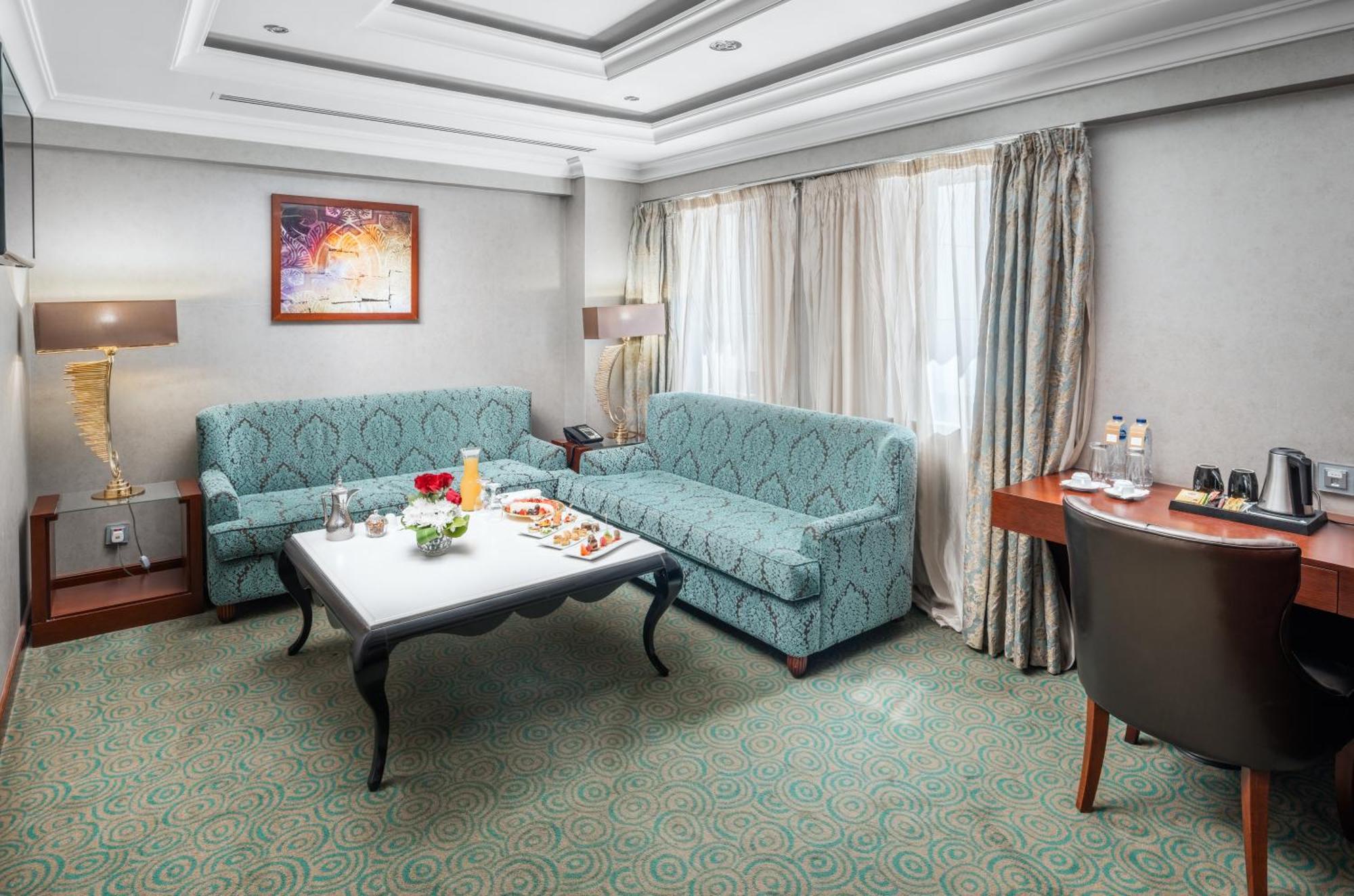 Al Aqeeq Madinah Hotel Médine Extérieur photo The photo shows a cozy hotel room or lounge area. It features two light blue sofas arranged around a low coffee table. On the table, there are snacks or refreshments arranged aesthetically. The room has a neutral color palette with a textured carpet 