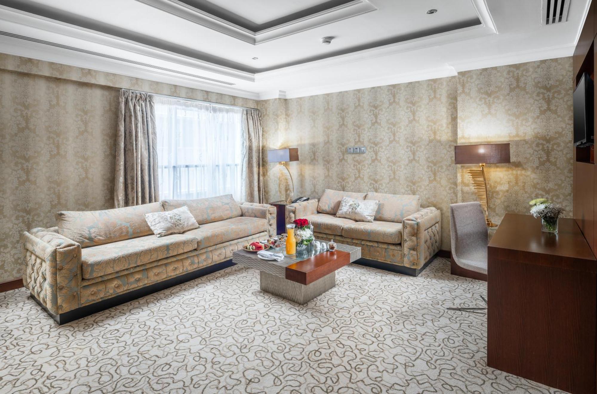 Al Aqeeq Madinah Hotel Médine Extérieur photo The photo shows a stylish living room with an elegant design. There are two beige sofas placed opposite each other, adorned with decorative pillows. A low coffee table is positioned in the center, featuring various items, possibly drinks or decorativ