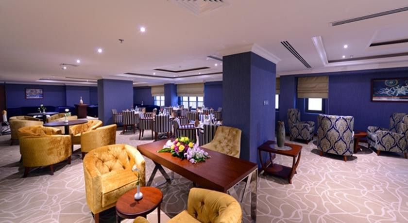 Al Aqeeq Madinah Hotel Médine Extérieur photo The photo shows a stylish interior of a restaurant or dining area. It features elegantly arranged seating with plush, gold-colored chairs and a wooden table at the center, adorned with a floral arrangement. The background includes more dining tables,