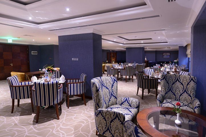 Al Aqeeq Madinah Hotel Médine Extérieur photo The photo shows an elegant dining or lounge area. The space features plush seating with striped and patterned chairs, and tables set up for dining. The decor includes a rich color palette with blue walls and soft lighting creating a warm atmosphere. 