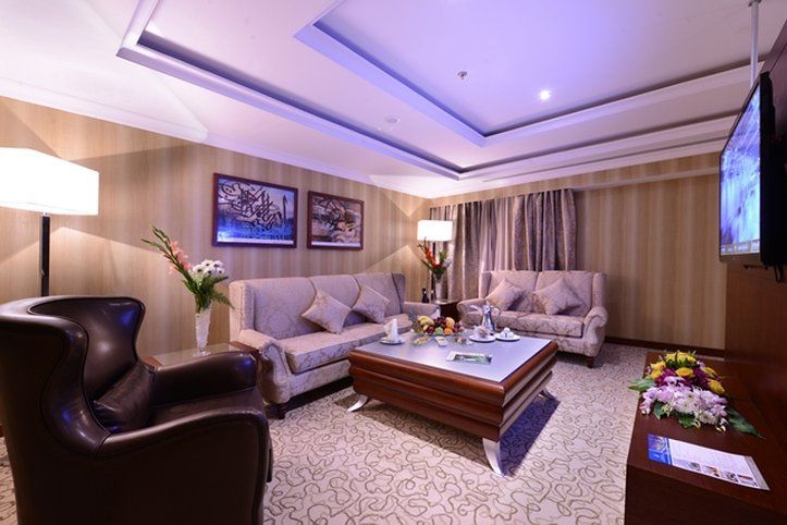 Al Aqeeq Madinah Hotel Médine Extérieur photo The photo shows a stylish and comfortable living room. It features two light-colored sofas with decorative cushions arranged around a modern coffee table. In one corner, there's a dark, leather armchair. The walls are adorned with framed artwork, and