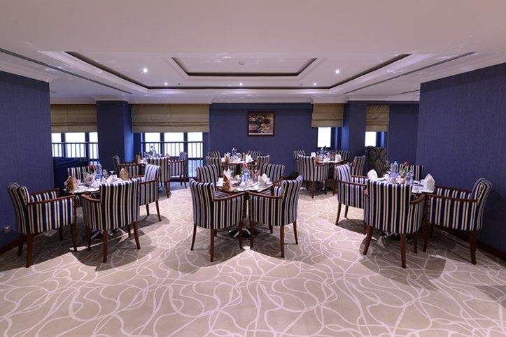 Al Aqeeq Madinah Hotel Médine Extérieur photo The photo shows an elegant dining room equipped with several tables. Each table is set with white tableware and neatly arranged silverware, giving a formal dining appearance. The decor features striped chairs and a carpet with a subtle pattern. The w