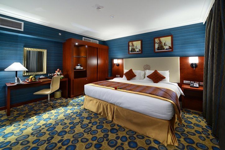 Al Aqeeq Madinah Hotel Médine Extérieur photo The photo shows a hotel room designed with a modern and stylish aesthetic. It features a large bed with a cream-colored headboard and decorative pillows. The room is decorated with blue walls and patterned carpet, creating a cozy atmosphere. 

There 